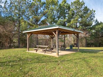 A picnic pavilion with a green roof is surrounded by trees.